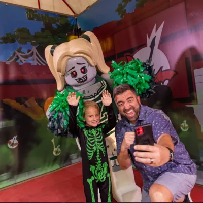 Father and Son taking photo with zombie cheerleader minifigure during Brick-or-Treat