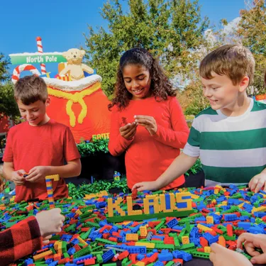 A photo of 3 children with a table of LEGO bricks with the word "Klaus" built.