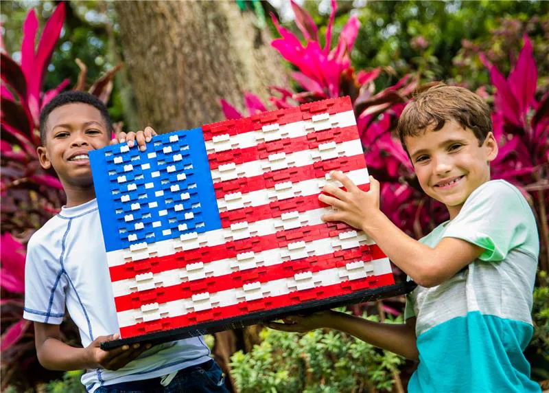 Two children posing with an American Flag made out of LEGO bricks