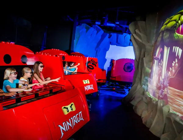 Guests wearing 3D glasses on the NINJAGO ride at LEGOLAND, using hand motions to battle a 3D snake on screen in interactive action.