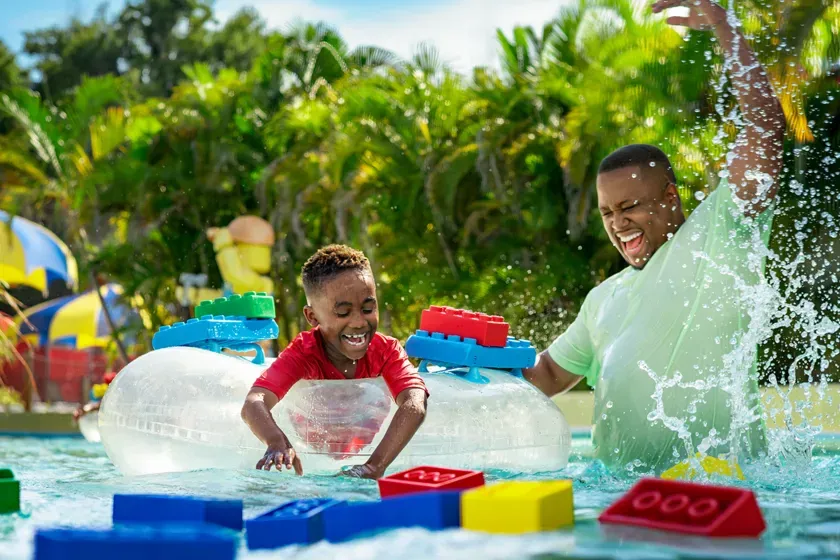 A parent and child splashing water together with LEGO-shaped floats