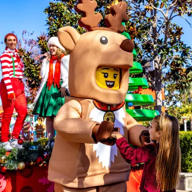 A child interacting with a LEGO reindeer character during a holiday celebration at LEGOLAND Resort, surrounded by festive decorations and performers